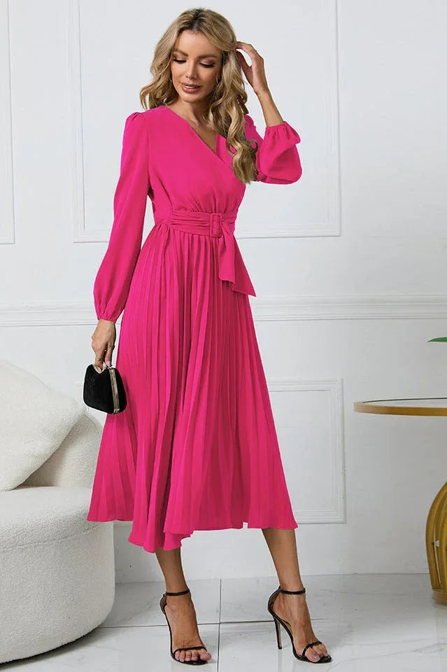Full-length view of a woman in a pink pleated midi dress with long sleeves.