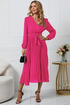Woman wearing a vibrant pink midi dress with a V-neck wrap front and accordion pleats.