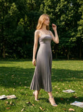 Woman wearing a gray satin midi dress with spaghetti straps and a square neckline, walking in a grassy park.