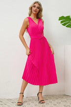 Woman in a pink pleated midi dress, showing the side profile and belt detail.