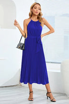 Woman wearing a royal blue pleated halter neck midi dress with a self-tie belt