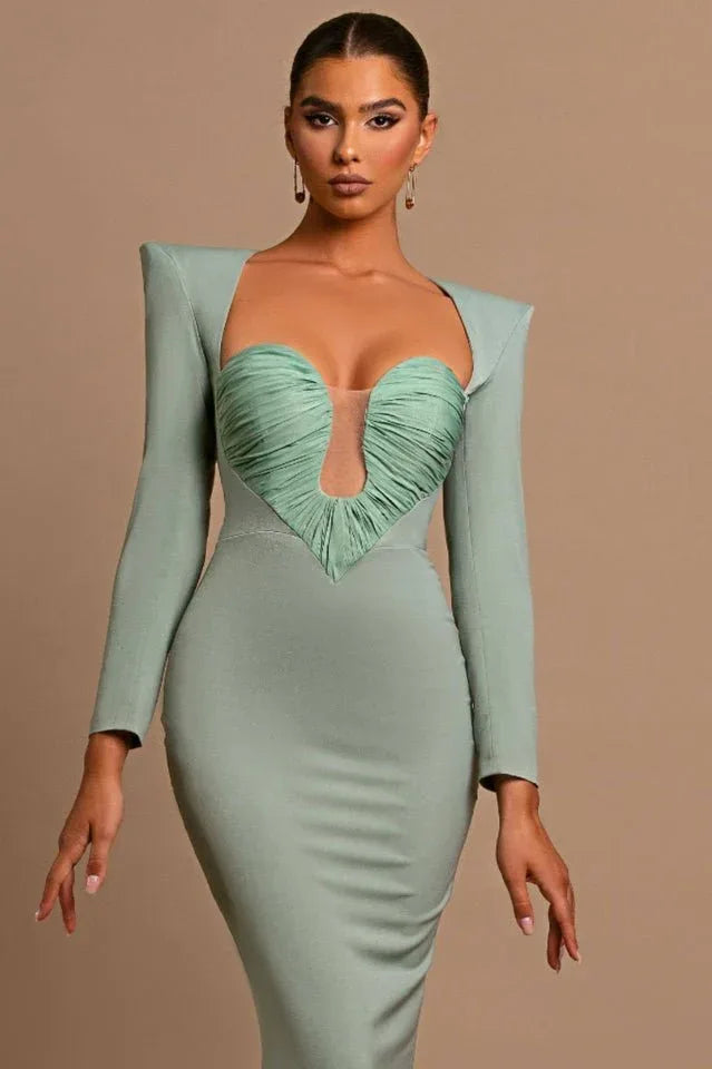 Model posing in a sage green formal gown with a dramatic neckline and fitted design.