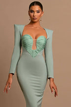 Model posing in a sage green formal gown with a dramatic neckline and fitted design.