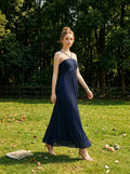 Woman in a navy blue pleated maxi dress with a halter neckline walking in a grassy field.