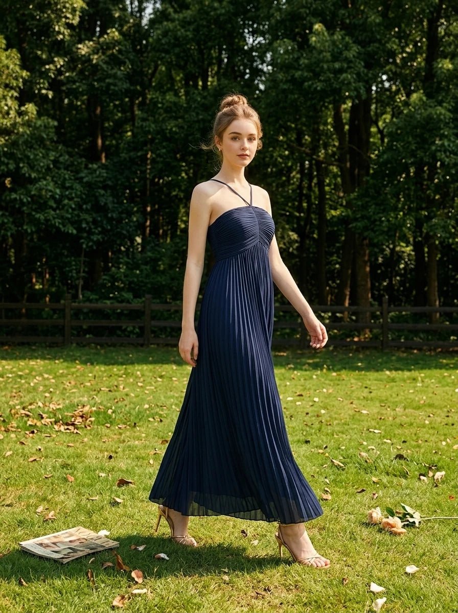 Woman in a navy blue pleated maxi dress with a halter neckline walking in a grassy field.