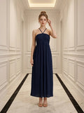 Woman in a navy blue pleated maxi dress with a halter neckline standing in a hallway.