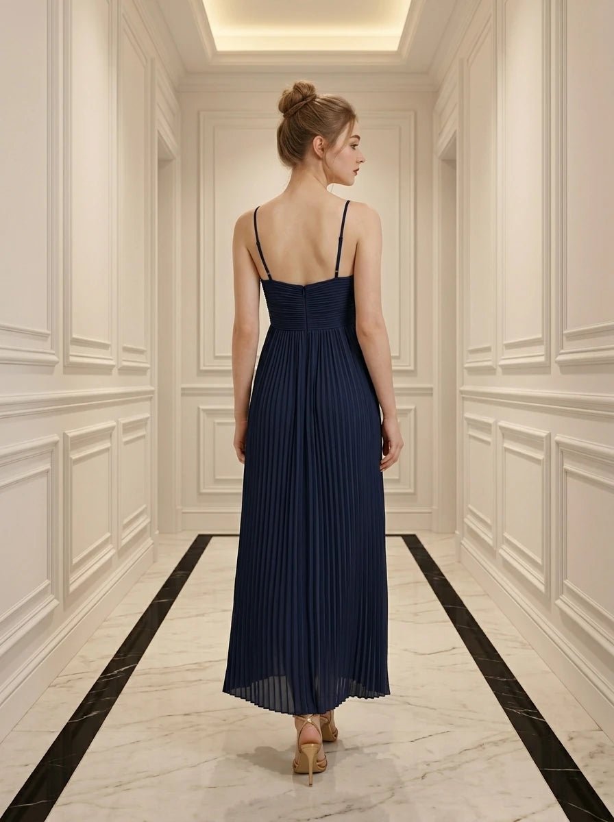 Back view of a woman in a navy blue pleated maxi dress with a halter neckline.