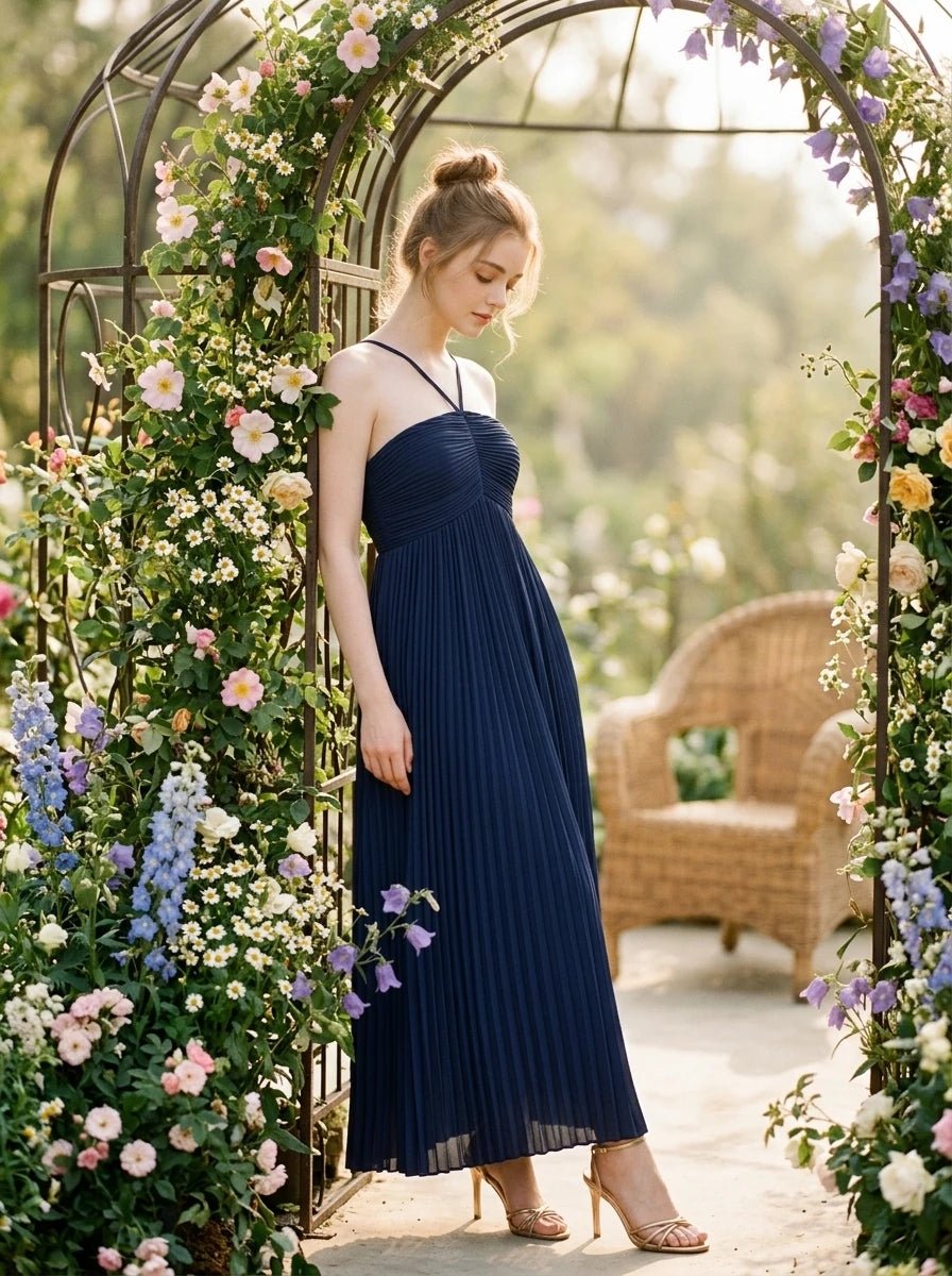 Woman in a navy blue pleated maxi dress with a halter neckline posing under a floral archway.