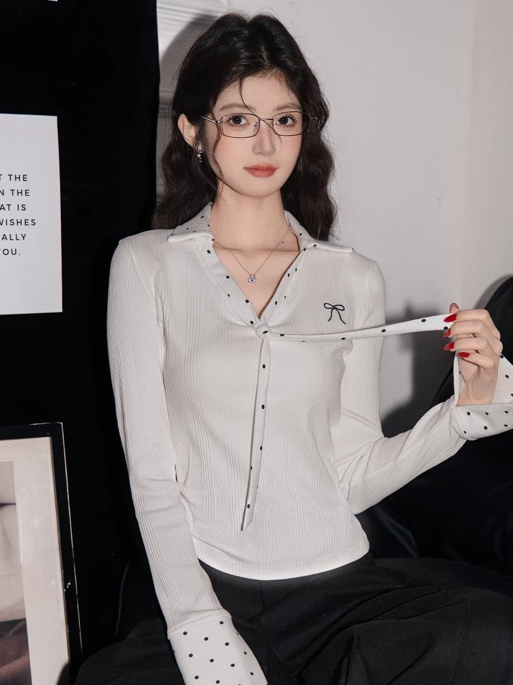 Woman wearing a white ribbed knit long-sleeve shirt with polka dot trim and a bow embroidery detail.