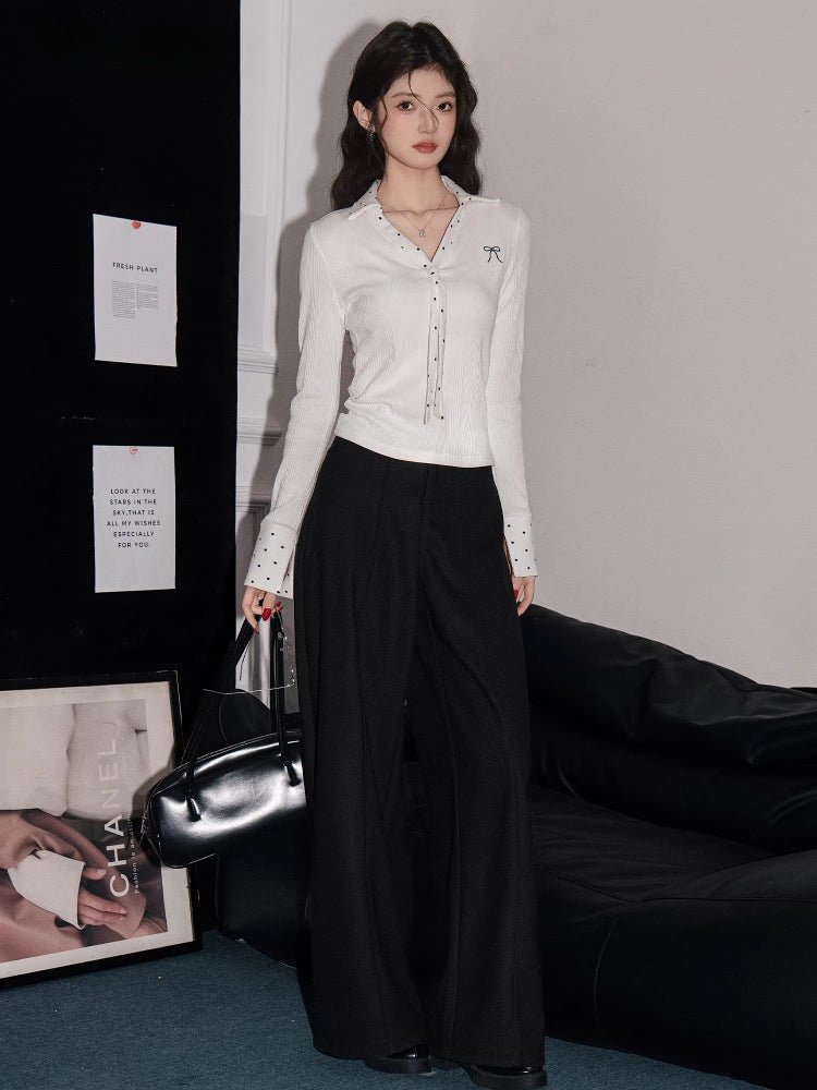 Full-body shot of the woman in a white ribbed knit shirt and black wide-leg pants, styled with a black handbag.