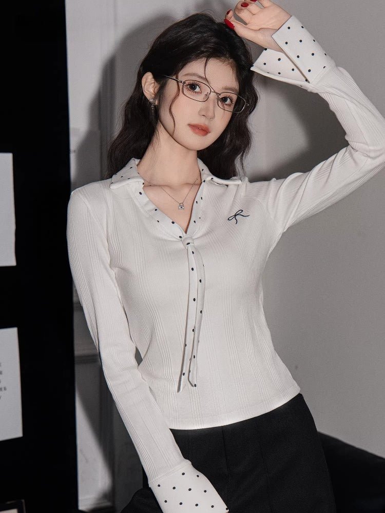Woman wearing a white ribbed knit long-sleeve shirt with polka dot trim and a bow embroidery detail.