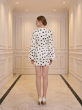 Back view of a woman in a white polka dot mini dress with plunging V-neck and bishop sleeves