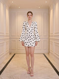 Woman wearing a white polka dot mini dress with plunging V-neck and bishop sleeves