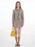Woman wearing a plaid collared shirt dress with an elasticated waist and long sleeves, holding a yellow handbag.
