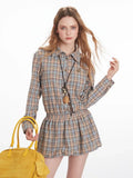 Front close-up of a woman wearing a plaid collared shirt dress with an elasticated waist and long sleeves, holding a yellow handbag.