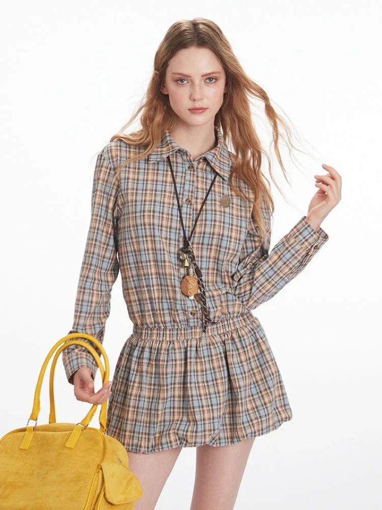 Front close-up of a woman wearing a plaid collared shirt dress with an elasticated waist and long sleeves, holding a yellow handbag.