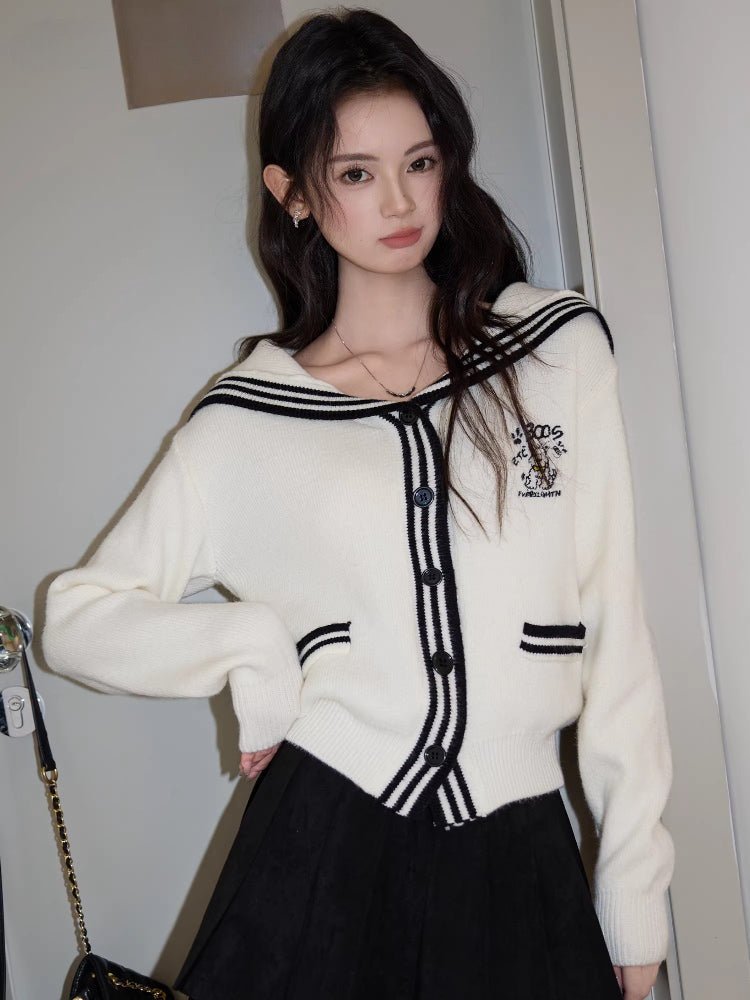 Woman wearing a cream knit cardigan with a navy sailor collar and trim, featuring button-up closure and embroidered graphic detail.