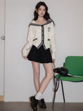 A woman styled in a cream knit cardigan with navy sailor collar and trim, offering a view of the outfit from the side.