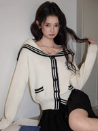 Close-up of a woman in a cream knit cardigan with navy sailor collar and trim, highlighting the button details and embroidery.
