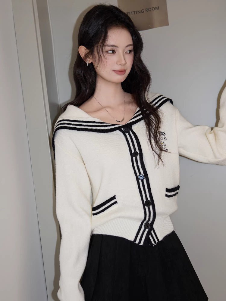 A woman poses in a cream knit cardigan with navy sailor collar and trim, showcasing the garment's silhouette.