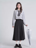Full body shot of a woman in a grey pinstripe blouse and black pleated skirt holding an umbrella