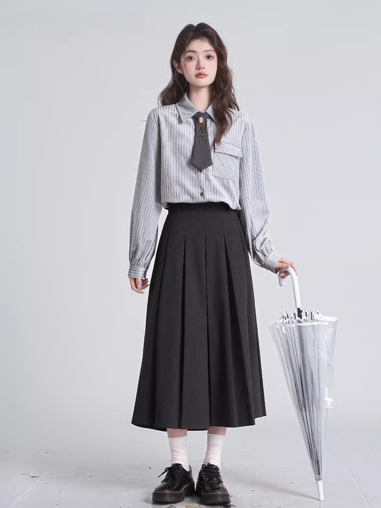 Full body shot of a woman in a grey pinstripe blouse and black pleated skirt holding an umbrella