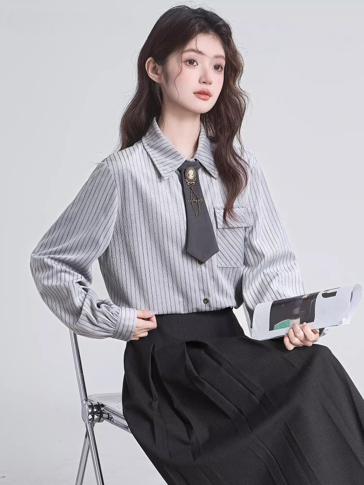 Woman sitting and holding a magazine while wearing a grey pinstripe blouse