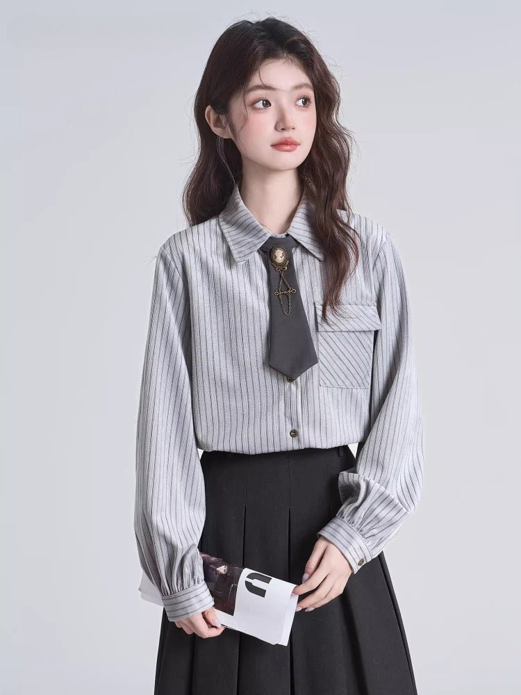 Woman wearing a grey pinstripe collared blouse with a dark grey tie and brooch accessory