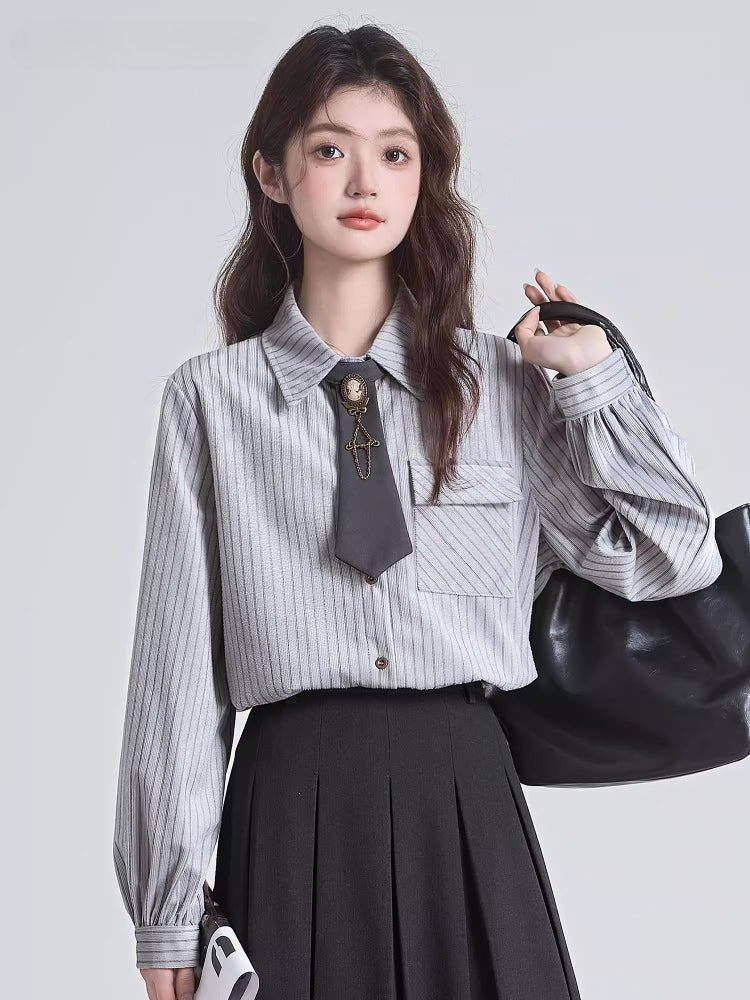 Woman wearing a grey pinstripe collared blouse with a dark grey tie and brooch accessory