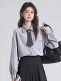 Woman wearing a grey pinstripe collared blouse with a dark grey tie and brooch accessory