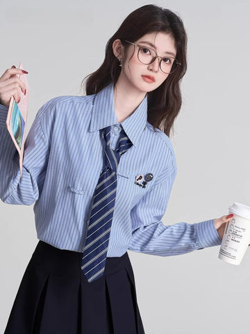 Woman wearing a light blue striped button-down shirt with a navy tie and glasses