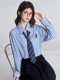 Full body shot of a woman in a light blue striped shirt, navy tie, and pleated skirt