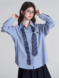 Close-up of a woman in a light blue striped shirt with a navy tie and embroidered patch