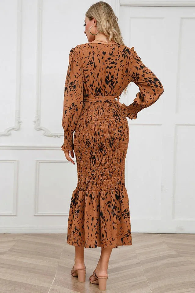 back view of a woman in a brown and black leopard print long sleeve smocked midi dress with a tie waist