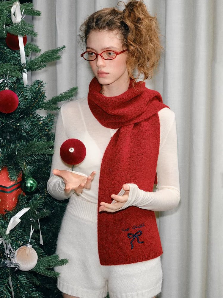 Model wearing a red knit scarf with an embroidered bow detail and text.