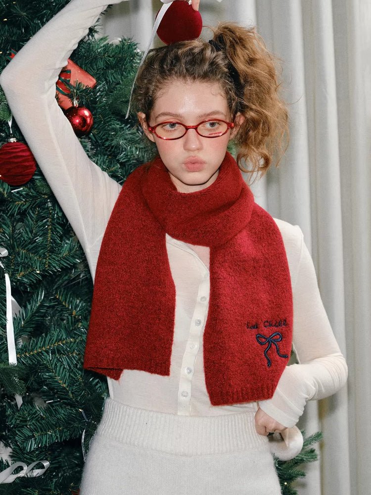 Model wearing a red knit scarf with an embroidered bow detail and text.