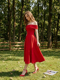 Woman in a red off-the-shoulder midi dress standing in a grassy area with trees.
