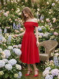 Woman in a red off-the-shoulder midi dress posing in a garden with flowers.