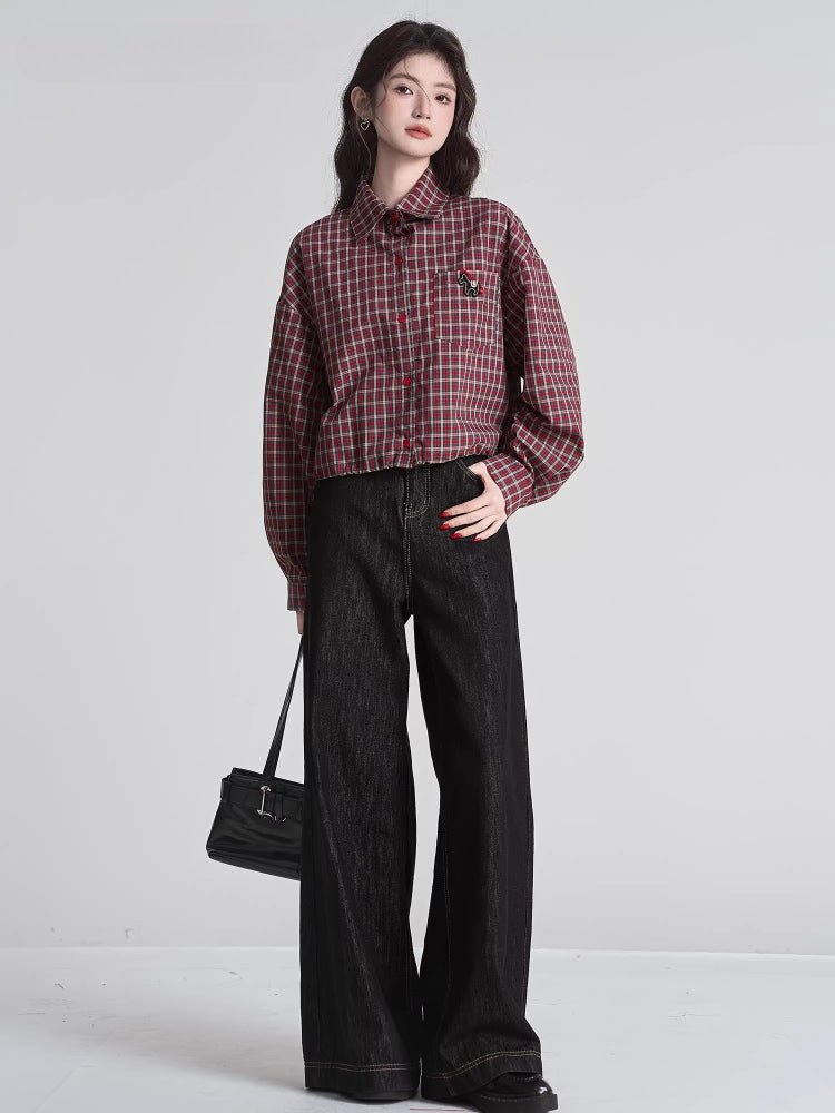 Full body shot of a woman wearing a red and beige plaid cropped shirt with wide-leg black jeans and a black handbag.