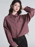 Woman wearing a red and beige plaid cropped shirt with a collared neckline and long sleeves.