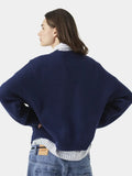Side view of a woman wearing a navy blue crewneck sweater and striped collared shirt.