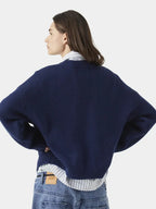 Side view of a woman wearing a navy blue crewneck sweater and striped collared shirt.