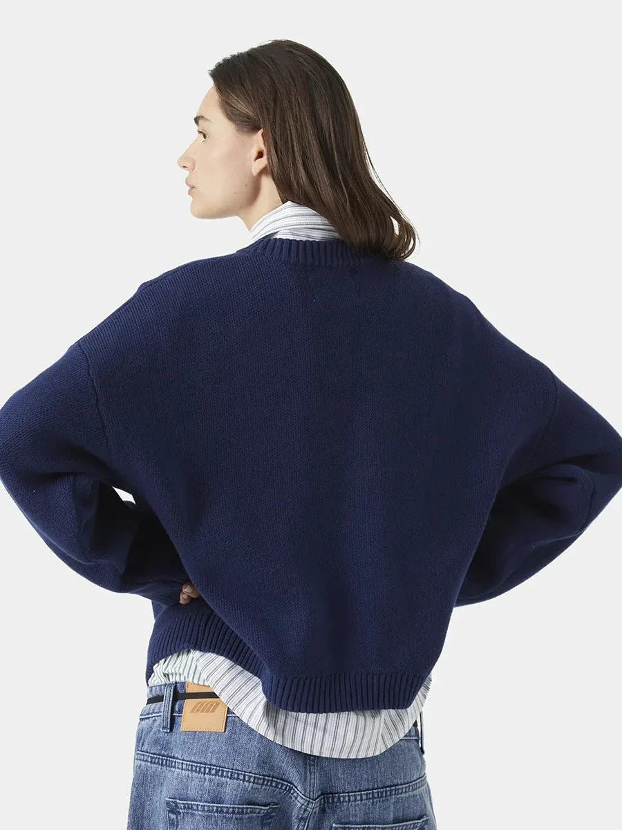 Side view of a woman wearing a navy blue crewneck sweater and striped collared shirt.