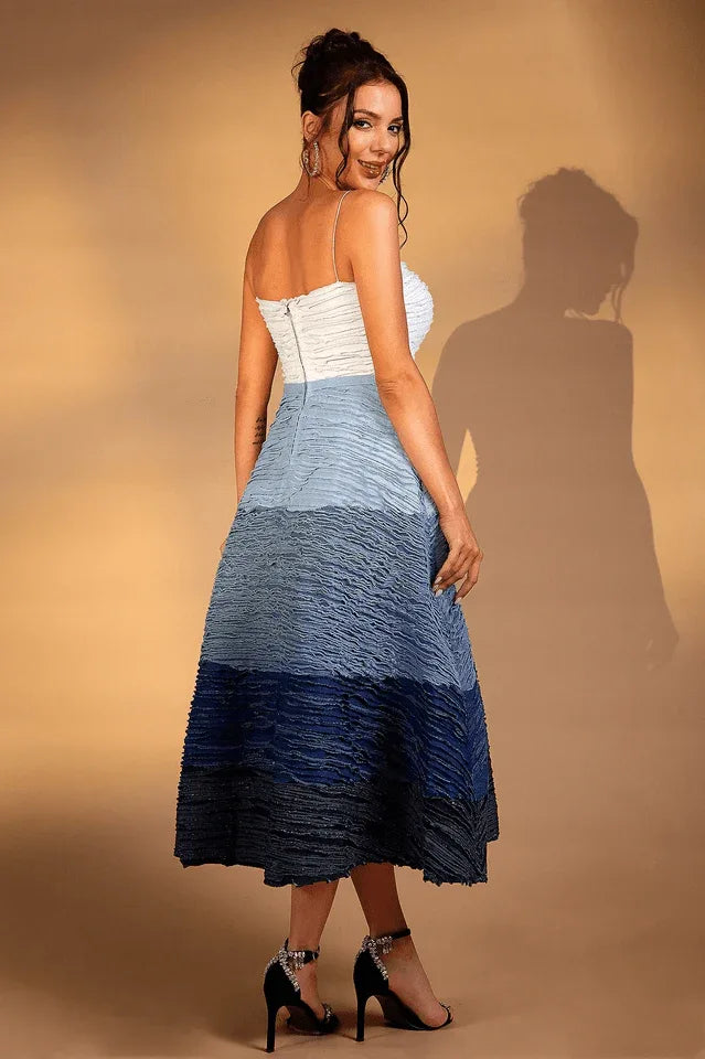 Back view of a woman in a white and blue ombre textured midi dress with a sweetheart neckline and spaghetti straps.