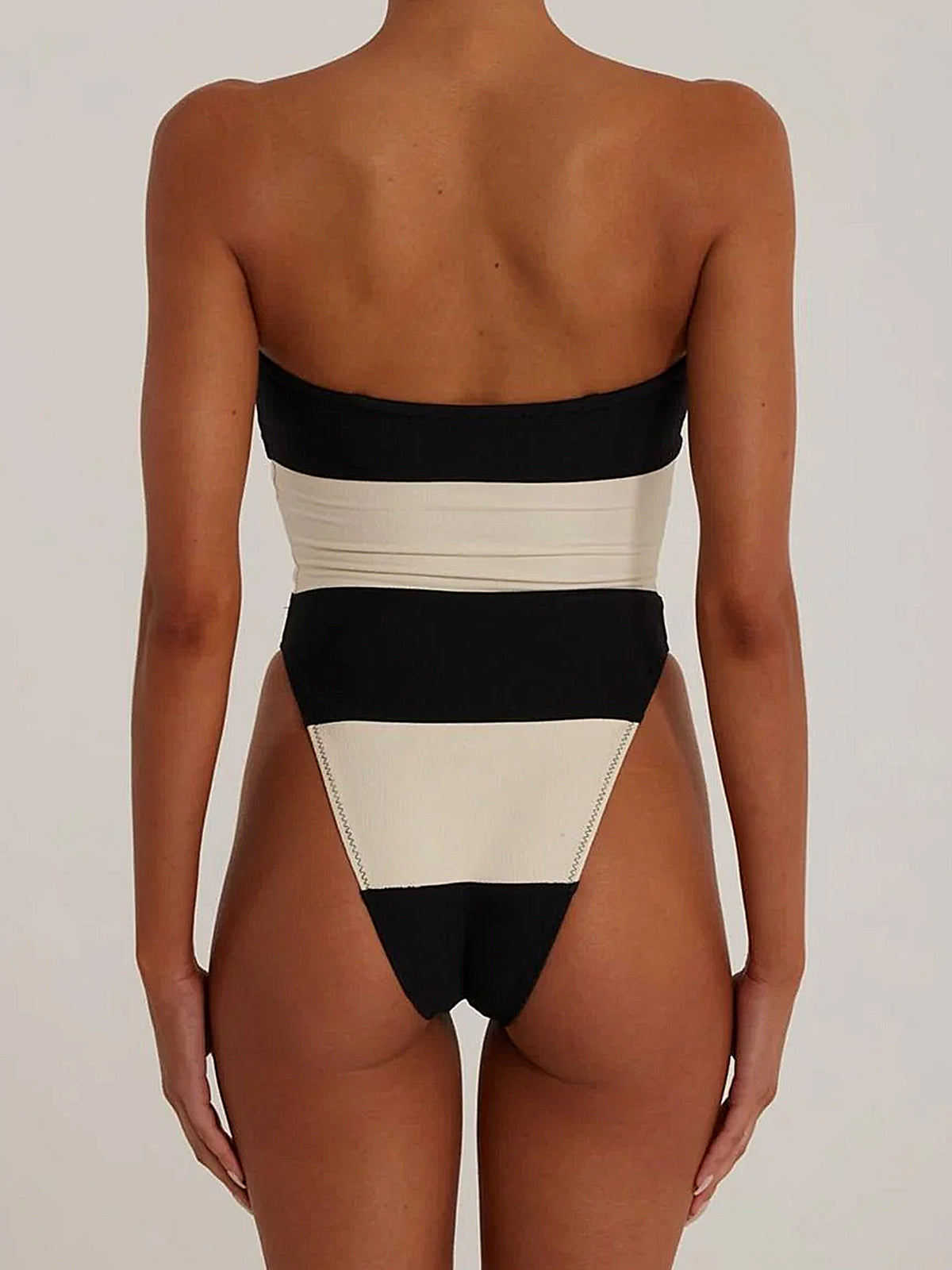Woman wearing a black and white striped strapless one-piece swimsuit, back view.