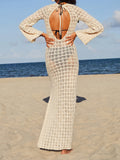 Back view of a woman in a cream crochet knit maxi dress with an open back and tie closure on a beach
