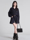 Full body shot of a woman in a dark wash denim shirt dress, brown belt, black boots, and a black handbag.