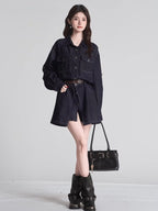 Full body shot of a woman in a dark wash denim shirt dress, brown belt, black boots, and a black handbag.