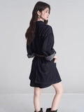 Rear view of a woman wearing a dark wash denim shirt dress with a brown belt and rolled sleeves.