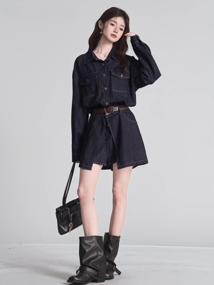 Woman standing in a dark wash denim shirt dress with a brown belt, black boots, and a black handbag slung over her shoulder.